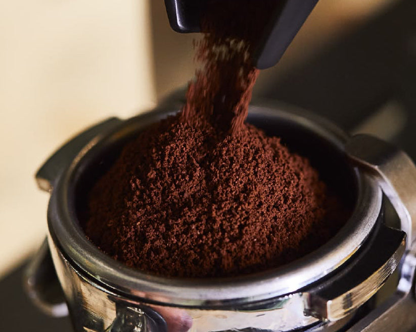 Close-up of coffee grounds being pressed into a coffee grinder.