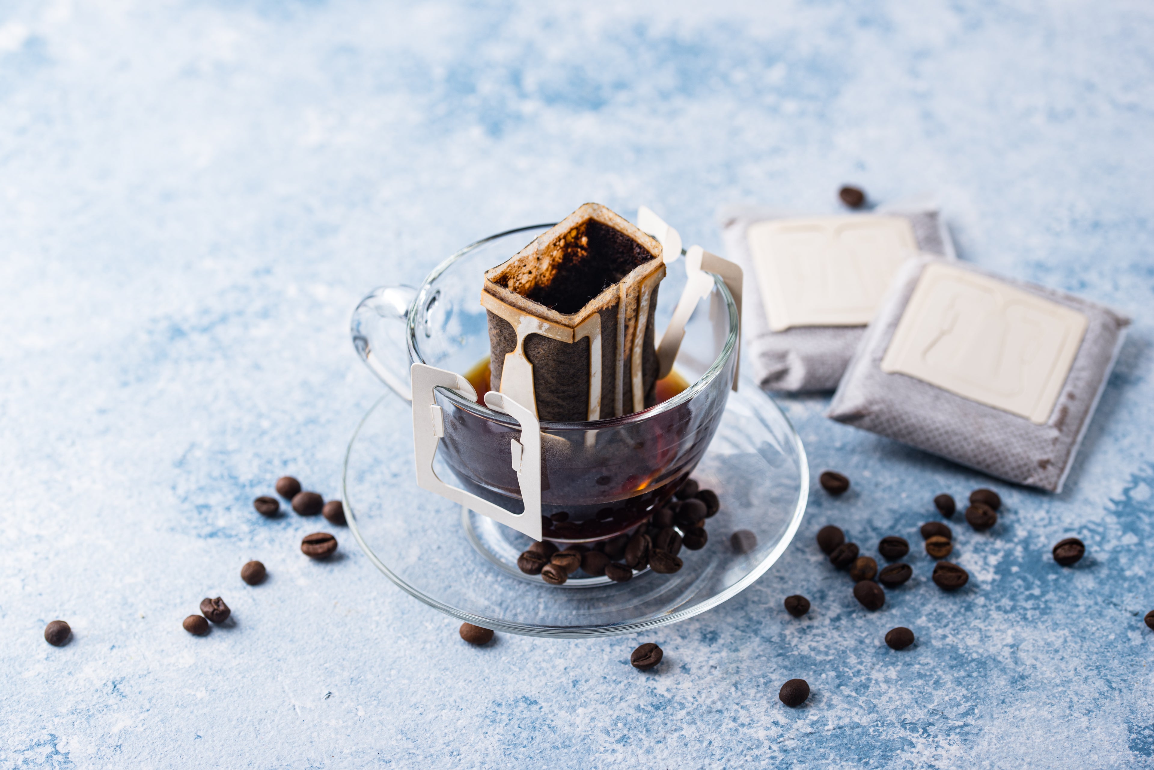 Drip coffee maker with coffee grounds and coffee beans on a light blue surface